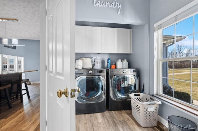 laundry area featuring washing machine and dryer, cabinet space, baseboards, and light wood finished floors