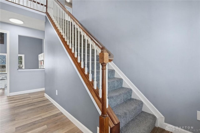 stairs featuring wood finished floors, baseboards, and a towering ceiling