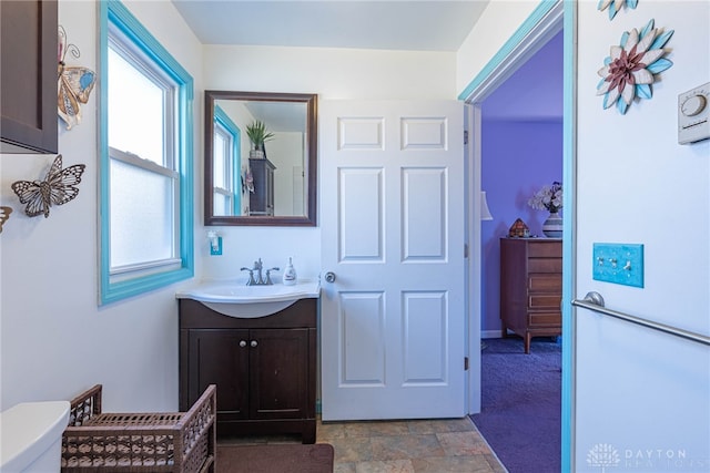 half bath with stone finish floor, vanity, and toilet