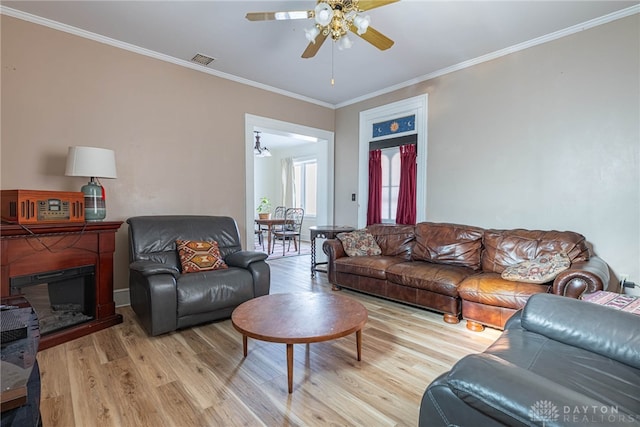 living area with visible vents, ornamental molding, a ceiling fan, light wood-style floors, and a fireplace