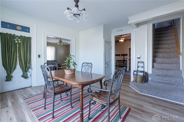 dining room featuring light wood-type flooring, ornamental molding, stairs, and a chandelier