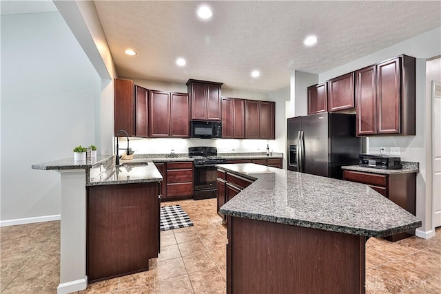 kitchen with dark stone countertops, a peninsula, black appliances, and a sink