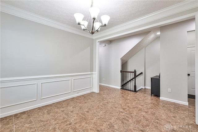 empty room with a textured ceiling, a decorative wall, a notable chandelier, and ornamental molding