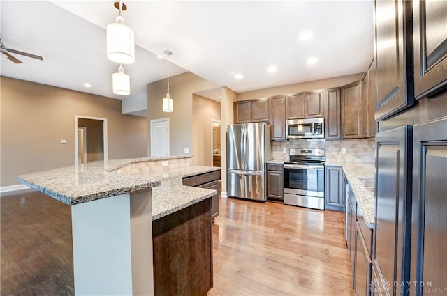 kitchen featuring a spacious island, light wood-style flooring, stainless steel appliances, decorative backsplash, and pendant lighting