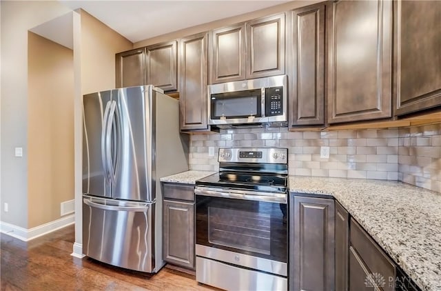 kitchen featuring light stone counters, tasteful backsplash, wood finished floors, stainless steel appliances, and baseboards