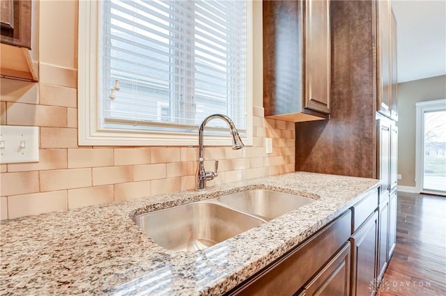 kitchen with a sink, light stone counters, tasteful backsplash, wood finished floors, and baseboards