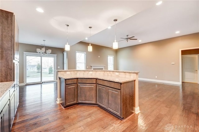 kitchen featuring light wood-style flooring, ceiling fan with notable chandelier, open floor plan, a center island, and baseboards