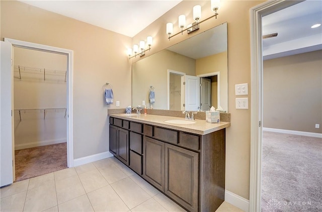 bathroom with double vanity, a walk in closet, baseboards, and a sink