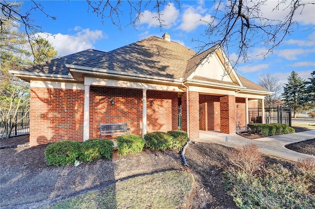 view of front facade featuring fence, brick siding, a chimney, and a shingled roof