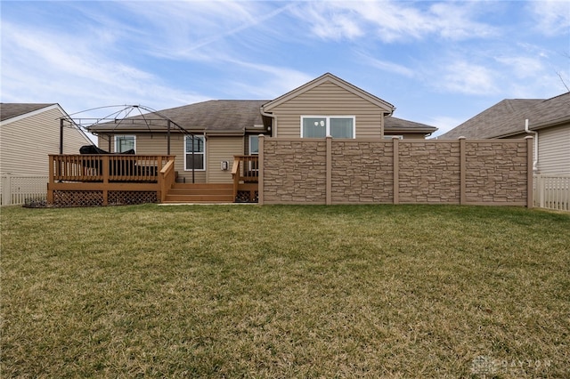 rear view of property featuring a lawn, a deck, stone siding, fence, and roof with shingles