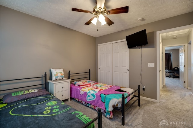 bedroom with a ceiling fan, a textured ceiling, a closet, baseboards, and light colored carpet