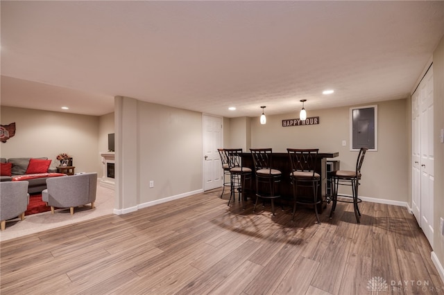 dining room featuring electric panel, wood finished floors, a bar, a fireplace, and baseboards