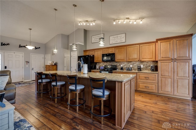 kitchen featuring a kitchen island with sink, a breakfast bar area, black appliances, and dark wood-style flooring