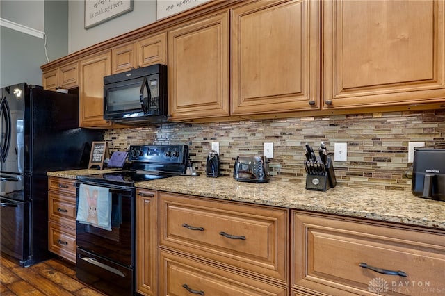 kitchen featuring light stone countertops, tasteful backsplash, black appliances, and dark wood-style floors