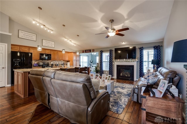 living room with a ceiling fan, lofted ceiling, dark wood-type flooring, rail lighting, and a glass covered fireplace