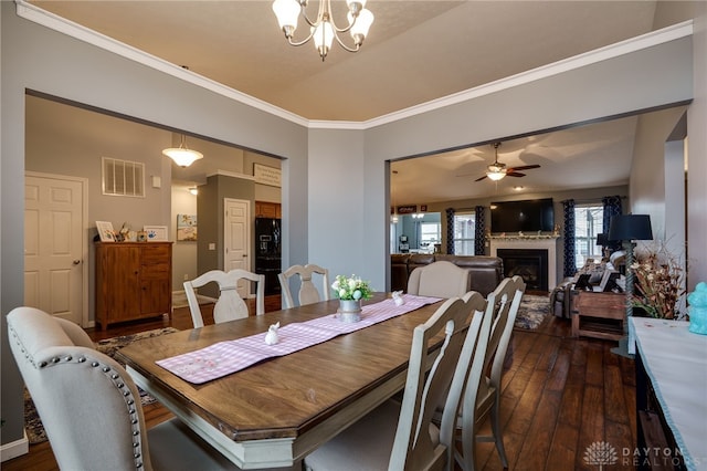 dining area with visible vents, a fireplace, dark wood-style flooring, ornamental molding, and ceiling fan with notable chandelier