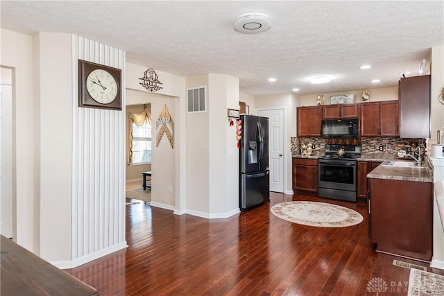 kitchen with visible vents, a sink, black appliances, dark wood-type flooring, and backsplash