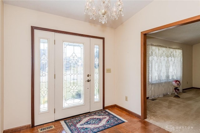 entrance foyer with baseboards, visible vents, carpet floors, lofted ceiling, and a chandelier