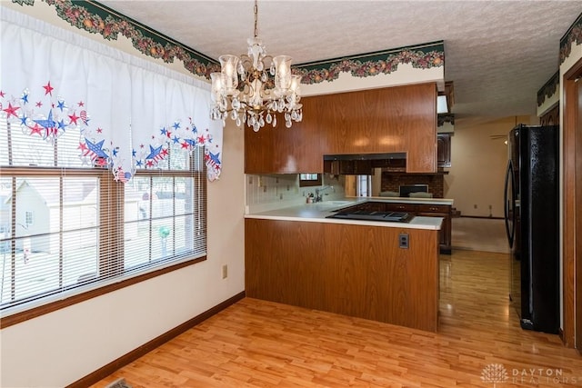 kitchen featuring light wood-style flooring, a peninsula, an inviting chandelier, brown cabinetry, and black appliances