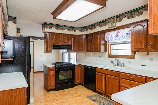 kitchen with a sink, black appliances, light countertops, and under cabinet range hood