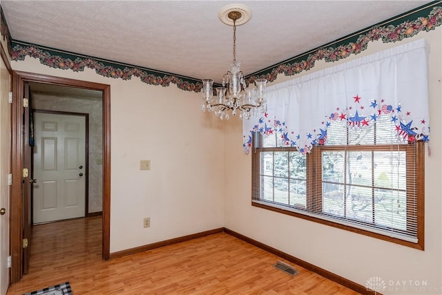 empty room with baseboards, visible vents, light wood finished floors, a textured ceiling, and a chandelier