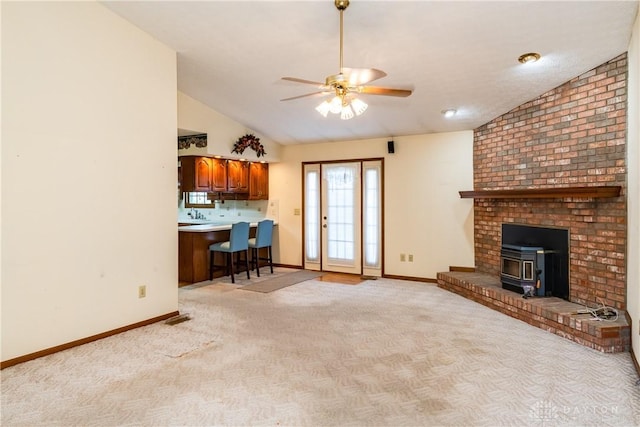 living area with baseboards, lofted ceiling, ceiling fan, and a wood stove