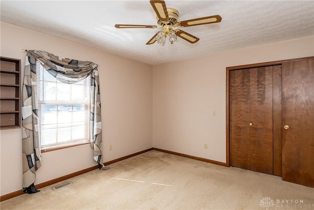 unfurnished bedroom featuring a ceiling fan, baseboards, visible vents, a closet, and light carpet