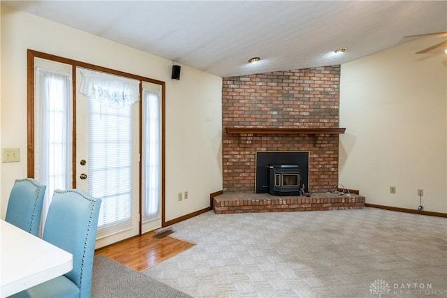 unfurnished living room with baseboards, lofted ceiling, carpet flooring, and a wood stove