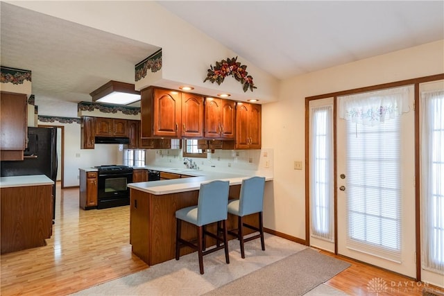 kitchen with black appliances, a sink, under cabinet range hood, a peninsula, and lofted ceiling