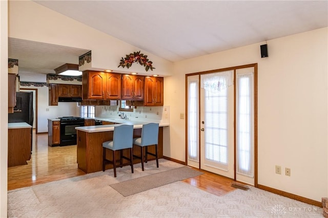 kitchen featuring black gas range oven, under cabinet range hood, vaulted ceiling, a peninsula, and a sink