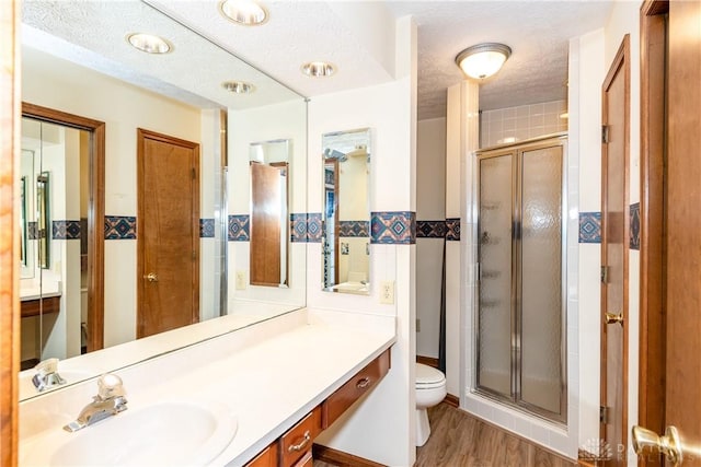 full bathroom featuring toilet, a stall shower, a textured ceiling, tile walls, and vanity