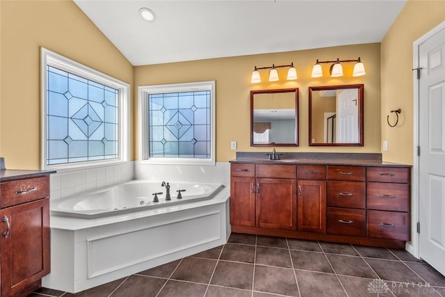 full bath with a jetted tub, vaulted ceiling, vanity, and tile patterned flooring