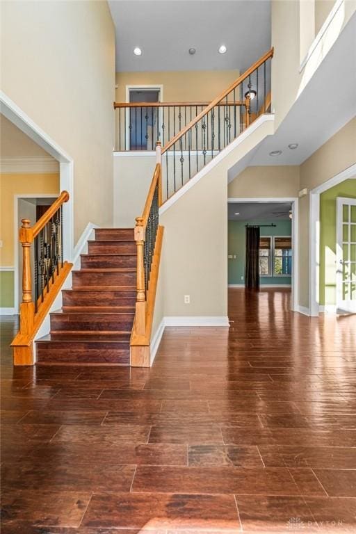 stairs featuring recessed lighting, wood finished floors, baseboards, and a towering ceiling