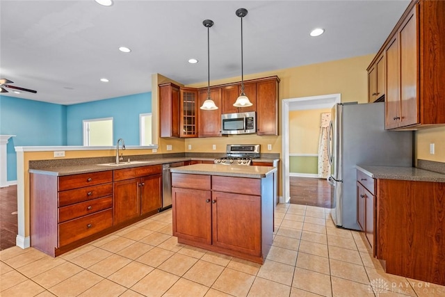 kitchen with a peninsula, light tile patterned flooring, a sink, stainless steel appliances, and a center island