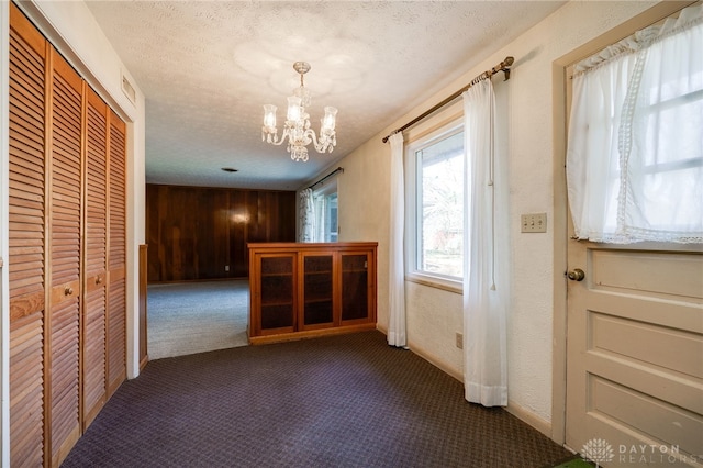 interior space featuring a chandelier, carpet flooring, a textured ceiling, and a textured wall