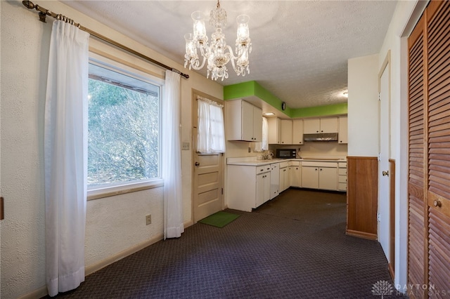 kitchen featuring under cabinet range hood, a textured ceiling, dark carpet, light countertops, and a textured wall