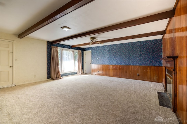 carpeted empty room with wooden walls, wallpapered walls, a wainscoted wall, beam ceiling, and a ceiling fan