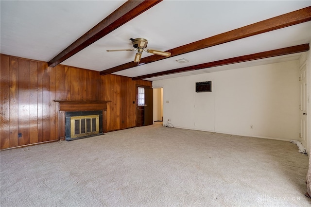 unfurnished living room featuring wooden walls, ceiling fan, beamed ceiling, carpet floors, and a glass covered fireplace