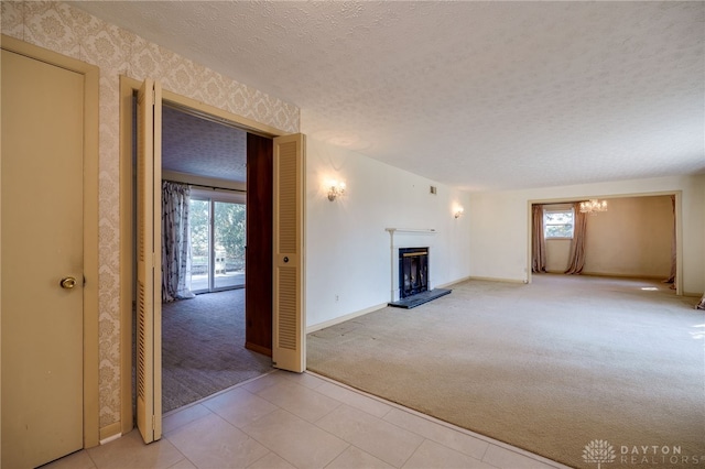 unfurnished living room with a wealth of natural light, light carpet, a textured ceiling, and a fireplace with raised hearth