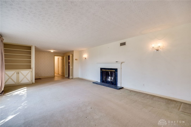 unfurnished living room featuring visible vents, carpet floors, a textured ceiling, and a fireplace with raised hearth