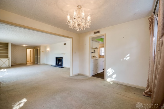 unfurnished living room with visible vents, a fireplace with raised hearth, light carpet, a textured ceiling, and washer / clothes dryer