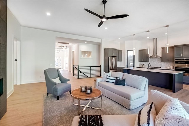 living area featuring recessed lighting, baseboards, light wood-style flooring, and ceiling fan with notable chandelier