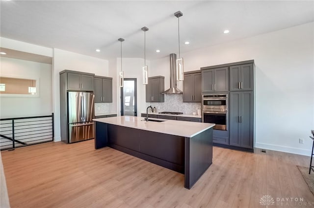 kitchen featuring light wood-style flooring, a sink, light countertops, appliances with stainless steel finishes, and wall chimney range hood