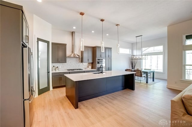 kitchen featuring tasteful backsplash, light countertops, stainless steel appliances, wall chimney exhaust hood, and a sink