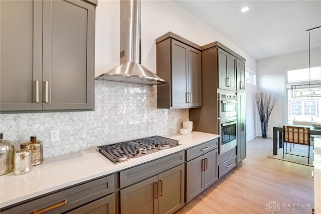 kitchen featuring light wood-type flooring, stainless steel appliances, light countertops, and wall chimney range hood