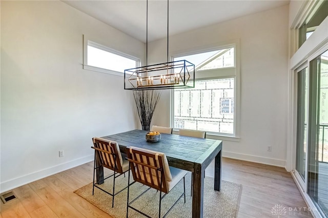 dining area featuring light wood-style flooring, a notable chandelier, baseboards, and visible vents