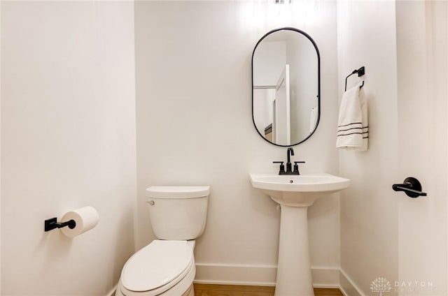 half bath featuring toilet, baseboards, and a sink