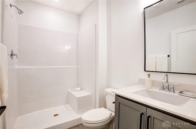 bathroom with visible vents, tiled shower, toilet, and vanity