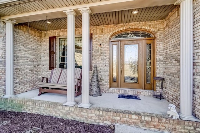 view of exterior entry with brick siding and a porch