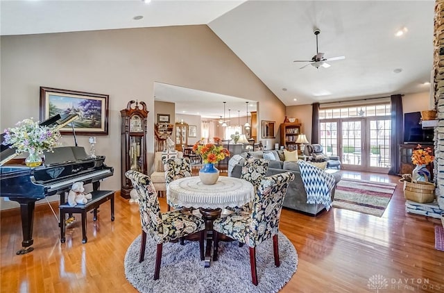 dining space featuring a fireplace, light wood-style flooring, a ceiling fan, and high vaulted ceiling